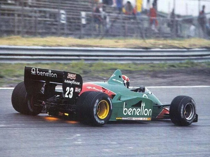Formule 1 Alfa Romeo v barvách Benettonu se startovním číslem 23 na mokré trati